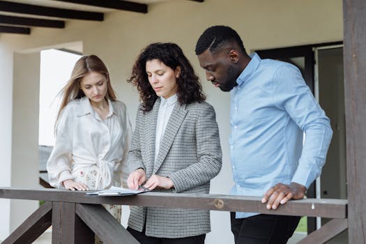 Three adults reviewing documents on a balcony during a real estate consultation.